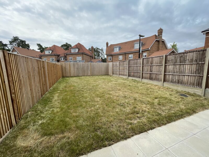 A new-build garden with long, dry grass and a patio.